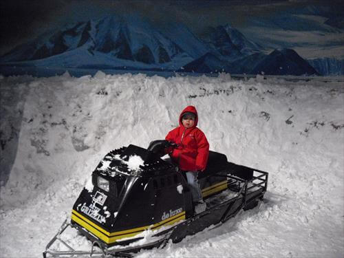 南極にいるような極寒、吹雪体験ルームでスノーモービルに乗っている男の子