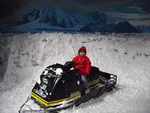 南極にいるような極寒、吹雪体験ルームでスノーモービルに乗っている男の子