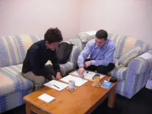 黄色と青の縞のソファーに座って英会話のレッスンを受けている男性とその先生