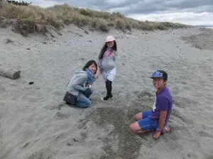 ニューブライトンの砂浜で砂遊びをするホームステイゲストと子供達