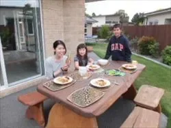 ホームステイ先の庭にあるアウトドアテーブルで食事をはじめようとしている女性と子供達