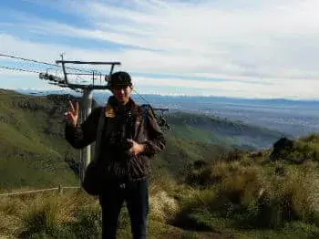 少し曇りがかかったクライストチャーチゴンドラ頂上の景色をバックに立つホームステイの男性