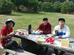 公園でおにぎりなどを食べてピクニックランチをしている３人